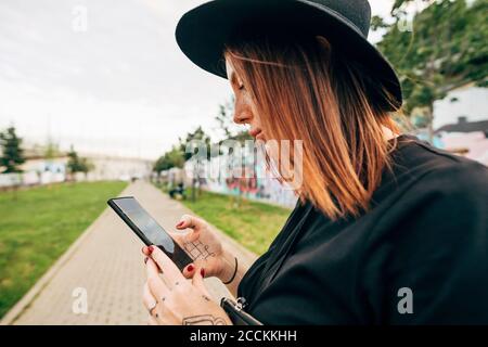 Primo piano di una giovane donna che indossa il cappello utilizzando lo smartphone parcheggio Foto Stock