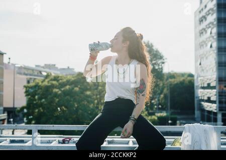 Donna che beve acqua mentre si siede sulla ringhiera all'aperto Foto Stock