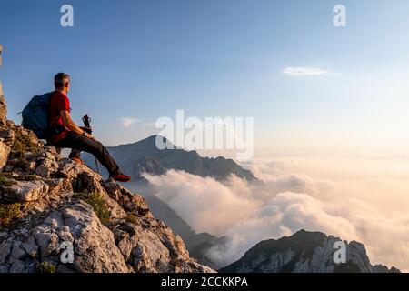 Escursionista ammirando la vista mentre si siede sulla cima della montagna alle Alpi Bergamasque, Italia Foto Stock