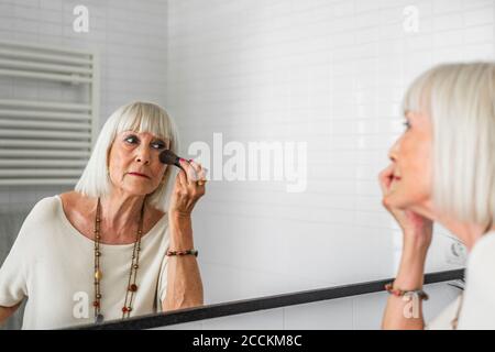 Donna anziana di stile che applica il trucco mentre guardando nello specchio a. casa Foto Stock