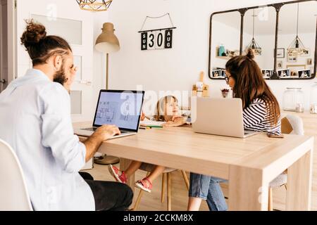 Uomo che lavora su un computer portatile mentre madre e figlia parlano sala da pranzo Foto Stock