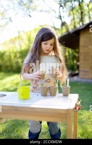 Carino ragazza che pianta semi in pentole piccole mentre si sta a. tavolo in cortile Foto Stock