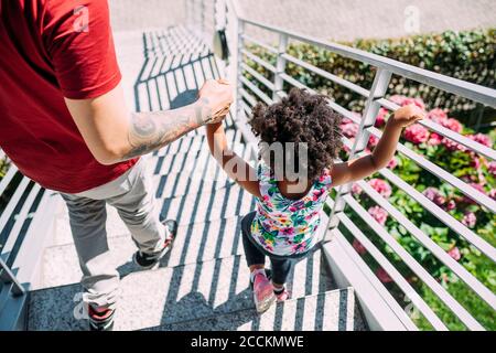 Il padre tiene le mani della figlia del bambino mentre si muove giù sui gradini Foto Stock