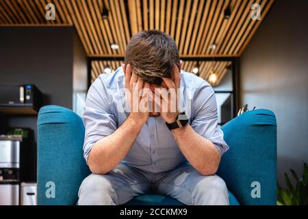 Uomo d'affari preoccupato con testa in mani seduta su poltrona a. caffetteria dell'ufficio Foto Stock