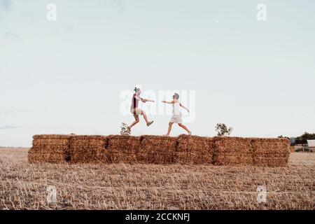 Coppia giocosa su balle di paglia contro il cielo limpido Foto Stock