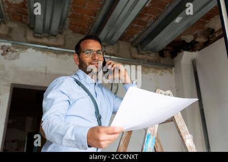 Ritratto di un architetto sicuro con piano al telefono in una casa in costruzione Foto Stock