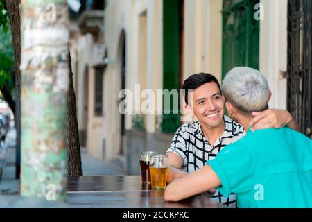 Una coppia gay che beve birra mentre si siede al tavolo in città Foto Stock