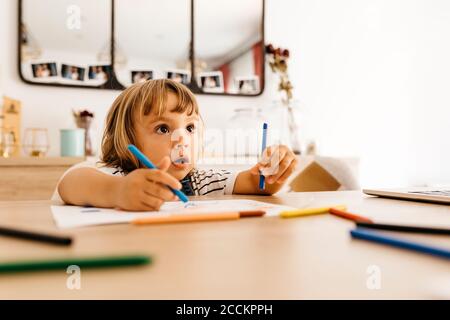 Ragazza carina che guarda via mentre dipingi su carta in pranzo camera a casa Foto Stock