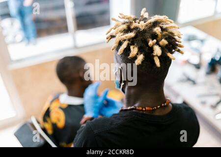 Barbiere con locs che taglia i capelli del cliente maschile in salone Foto Stock