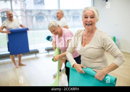 Donna anziana ridente che rotola il tappetino dopo la lezione di yoga Foto Stock