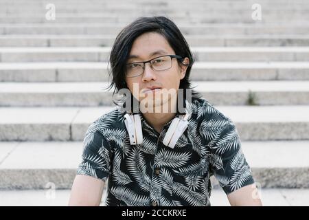 Primo piano di un giovane uomo che indossa gli occhiali con le cuffie appoggiate passi in città Foto Stock