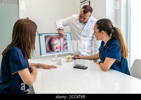 Dentista che discute con medici di sesso femminile mentre si guarda ai raggi X. in clinica Foto Stock