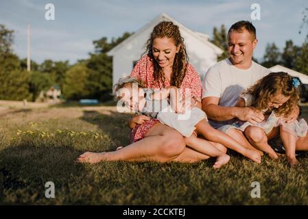 Felici genitori con due figlie seduti su un prato dentro davanti alla loro casa Foto Stock