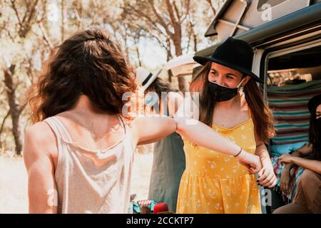 Donne con maschere protettive salutano con ellbow durante il camper viaggio Foto Stock