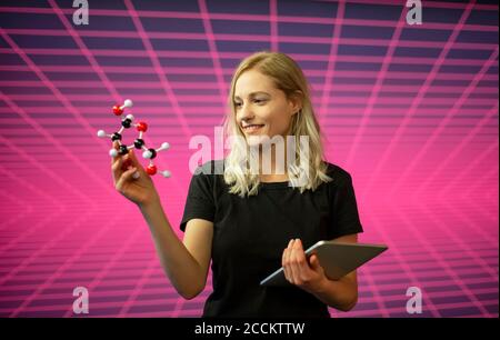 Donna scienziata che tiene in piedi un modello molecolare e un tablet digitale rispetto al modello a griglia Foto Stock