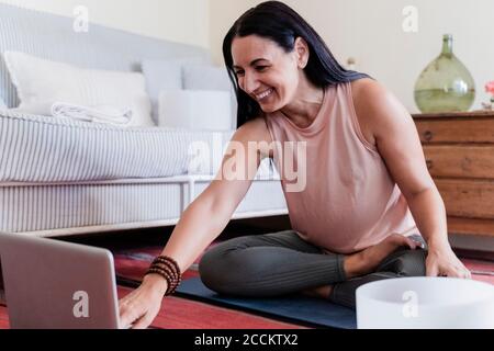 Donna matura sorridente di fronte al computer portatile a casa Foto Stock