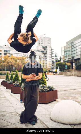 MAM che salta su un amico maschile utilizzando il telefono in città Foto Stock