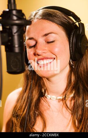 Cantante con cuffie al microfono in studio di registrazione Foto Stock