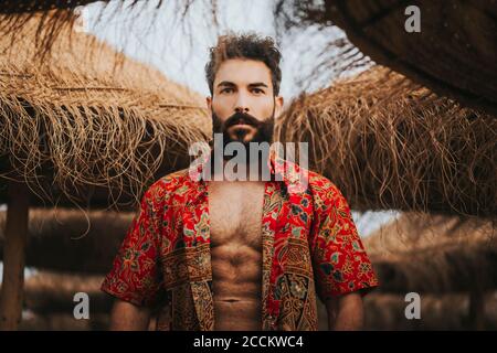 Attraente uomo bearded con camicia colorata in piedi tra ombrelloni da spiaggia Foto Stock