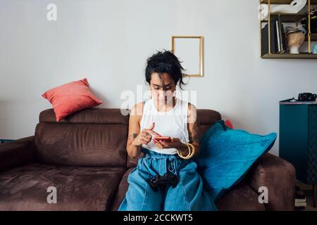 Donna che utilizza il telefono cellulare sul divano nel soggiorno Foto Stock