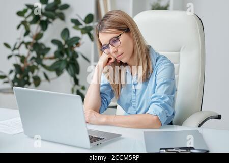 Giovane donna d'affari stanca con capelli biondi che guarda inffelicemente al laptop display Foto Stock
