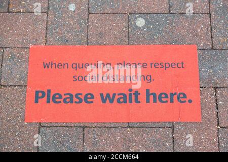 Un cartello a terra all'esterno di un supermercato che mostra i clienti dove fare la coda per conformarsi alle linee guida di distanziamento sociale Foto Stock