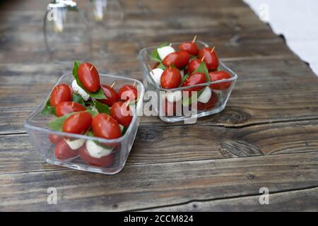 Primo piano di pomodori ciliegini rossi con basilico fresco e mozzarella. Antipasti cosparsi di sale e pepe, serviti su piccoli piatti di vetro quadrati Foto Stock