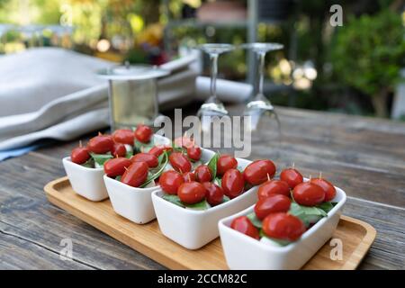 Primo piano di pomodori ciliegini rossi con basilico fresco e mozzarella. Antipasti cosparsi di sale e pepe, serviti su un piccolo plat rettangolare bianco Foto Stock