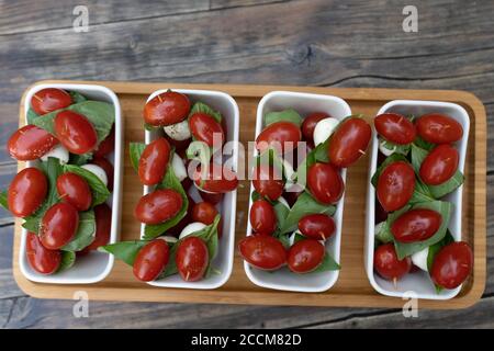 Primo piano di pomodori ciliegini rossi con basilico fresco e mozzarella. Antipasti cosparsi di sale e pepe, serviti su un piccolo plat rettangolare bianco Foto Stock