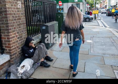 Londra - Agosto 2020: Una donna passa davanti a un uomo senza casa con un cane per le strade di Chelsea Foto Stock