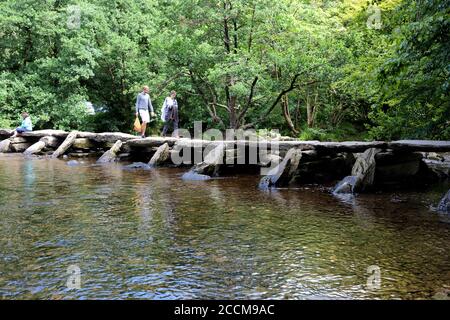 Gli escursionisti attraversano il ponte del clapper noto come Tarr Steps on Il fiume Barle nel parco nazionale di Exmoor, Somerset Foto Stock