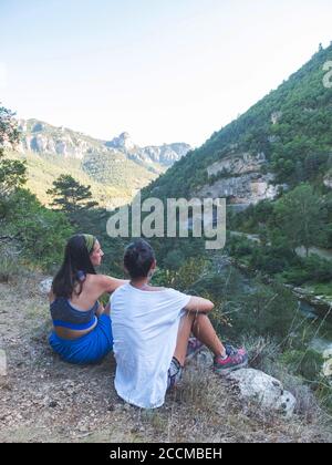 Due amici donne seduti sulle rocce, pietre sulla collina e ammirando la splendida vista delle verdi colline e montagne Foto Stock