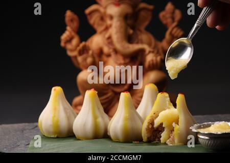 Modak - piatto tradizionale preparato con il festival di Ganpati in India, servito con burro chiarificato. Idolo Ganesh sullo sfondo Foto Stock