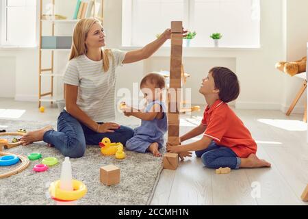 Mamma e figli stanno costruendo una torre di cubetti di legno nella stanza. La madre insegna ai bambini la giornata fuori a casa. Foto Stock