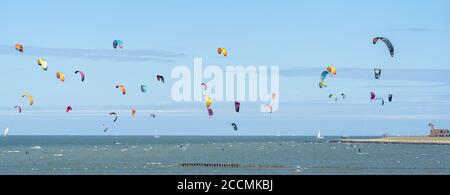 Gruppo di kite surfisti con brillanti aquiloni colorati che praticano il loro sport in mare sotto un cielo blu Foto Stock