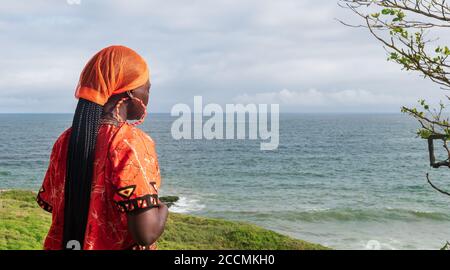 Donna Africana in preghiera con abito tradizionale arancione da Ghana sguardi Al di sopra dell'orizzonte a Takoradi Ghana Africa Occidentale Foto Stock