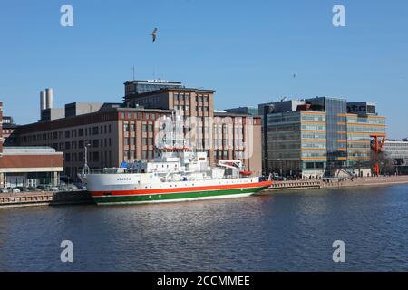 Imbarcazione nautica a strisce arancioni e verdi ormeggiata a Salmisaari, Helsinki, Finlandia, di fronte all'ex fabbrica di cavi, oggi spazio culturale Foto Stock