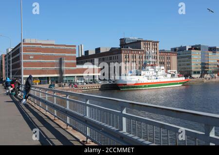 Imbarcazione nautica a strisce arancioni e verdi ormeggiata a Salmisaari, Helsinki, Finlandia, di fronte all'ex fabbrica di cavi, oggi spazio culturale Foto Stock