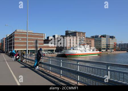 Imbarcazione nautica a strisce arancioni e verdi ormeggiata a Salmisaari, Helsinki, Finlandia, di fronte all'ex fabbrica di cavi, oggi spazio culturale Foto Stock