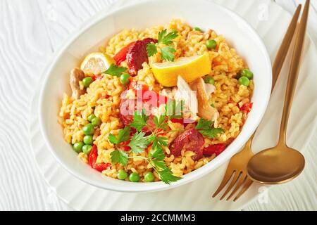 porzione di paella di pollo spagnola con riso valenciano bomba, coscia di pollo, salsicce chorizo, verdure e spezie servite su un piatto bianco su a. Foto Stock