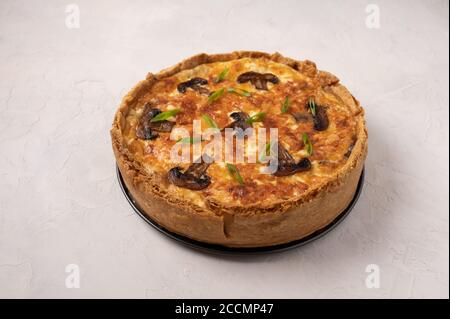 Quiche tradizionali francesi a torta con funghi e formaggio su uno sfondo chiaro testurizzato, primo piano, spazio di copia Foto Stock