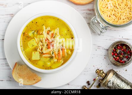 Zuppa di pollo con patate, carote e pasta Orzo in un piatto bianco su un tavolo di legno. Minestrone. Cucina mediterranea (italiana). Messa a fuoco selettiva Foto Stock