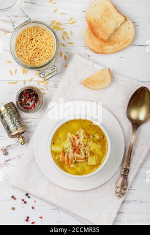 Zuppa di pollo con patate, carote e pasta Orzo in un piatto bianco su un tavolo di legno. Minestrone. Cucina mediterranea (italiana). Messa a fuoco selettiva Foto Stock