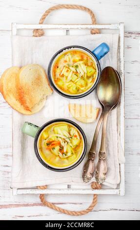 Zuppa di pollo con patate, carote e pasta Orzo in tazze di ceramica su un tavolo di legno. Minestrone. Cucina mediterranea (italiana). Messa a fuoco selettiva Foto Stock