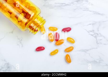 Vitamine. Pillole multicolore (rosso e arancione) (dragee) in una bottiglia gialla su un tavolo di marmo. Il concetto di salute. Messa a fuoco selettiva, vista superiore e copia Foto Stock