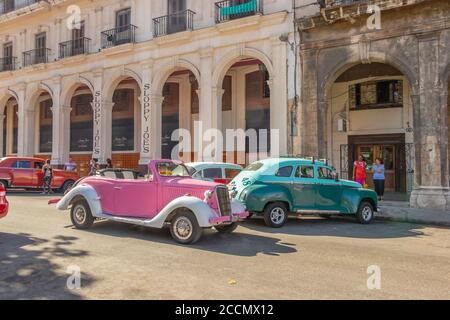 Auto d'epoca colorate parcheggiate in una strada vivace di fronte a edifici storici con persone che camminano per l'Avana cuba Foto Stock