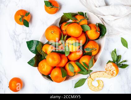 Fresco biologico agrumi mandarino arance frutta (tangerini, clementine) con foglie in un piatto leggero su sfondo marmoreo. Messa a fuoco selettiva, vista dall'alto AN Foto Stock