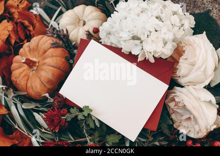 Autunno ancora vita. Biglietto d'auguri vuoto, busta mock-up. Mums, rose rosa e fiori di idrangea. Zucche bianche e arancioni, rami vivi. Vendemmia Foto Stock