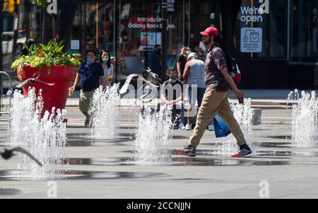 Toronto, Canada. 23 agosto 2020. Un uomo cammina attraverso le fontane in Yonge-Dundas Square a Toronto, Canada, il 23 agosto 2020. Ambiente Canada ha emesso un avvertimento di calore per Toronto con le temperature previste per salire nei 30 bassi la Domenica e Lunedi. Credit: Zou Zheng/Xinhua/Alamy Live News Foto Stock