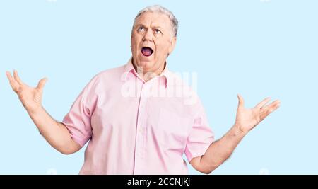 Uomo anziano con capelli grigi che indossa abiti casual pazzo e pazzo gridando e urlando con espressione aggressiva e le braccia sollevate. Concetto di frustrazione. Foto Stock